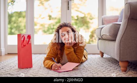 Femme en pull chaud confortable couché sur le sol à la maison écriture carte de voeux ou lettre Banque D'Images