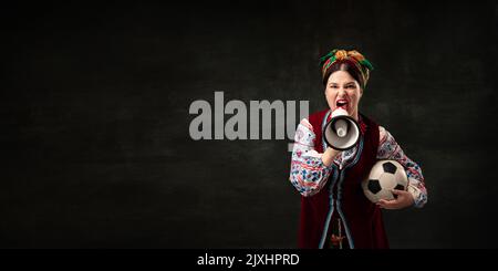 Flyer avec une jeune femme expressive en costume national traditionnel ukrainien criant au mégaphone isolé sur fond sombre vintage. Sport Banque D'Images