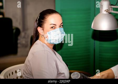 Jeune podiatre femelle avec un masque protecteur regardant la caméra dans sa clinique de podiatrie Banque D'Images