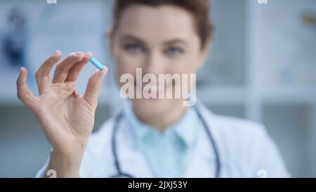 docteur flou et gai dans un manteau blanc souriant tout en tenant capsule, image de stock Banque D'Images