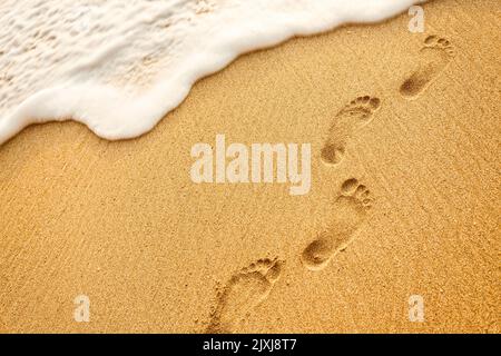 Plage, vagues et traces de pieds au coucher du soleil Banque D'Images