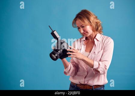 Photographe femelle mature avec caméra sur fond bleu sur prise de vue en studio Banque D'Images