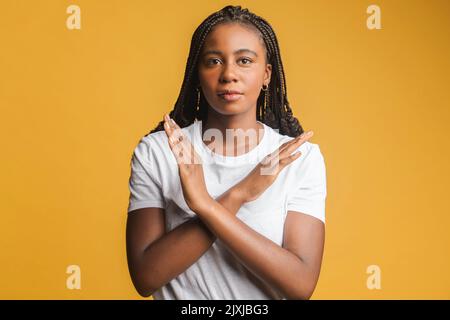 Jamais, aucun compromis. Portrait d'une femme hipster insatisfaite avec des cheveux fantaisie croisant les mains, montrant x signe, interdiction ou geste d'interdiction, rejetant l'offre. studio tourné isolé sur fond jaune Banque D'Images