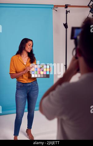 Modèle femelle mature posant contre l'arrière-plan sur une prise de vue en studio tenant une carte de vérification des couleurs pour la vidéo Banque D'Images