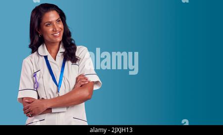 Portrait d'une infirmière mature féminine souriante portant un uniforme debout devant un arrière-plan de studio bleu Banque D'Images