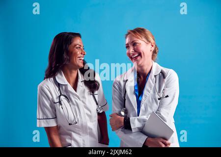 Médecin et infirmière mature portant un manteau blanc riant et parlant devant le Blue Studio arrière-plan Banque D'Images