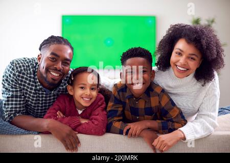 Portrait de famille assis sur un canapé regarder un film sur un téléviseur à écran vert à la maison Banque D'Images