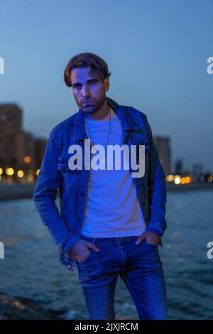 Portrait d'un homme caucasien posant portant une veste et un pantalon jean avec un éclairage bleu à la lumière du coucher du soleil. Banque D'Images