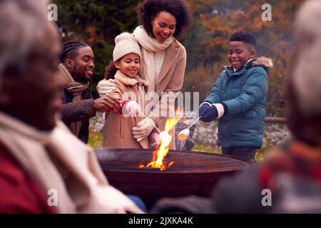 Famille multi-génération ayant plaisir à toaster les guimauves dans le jardin d'automne ensemble Banque D'Images