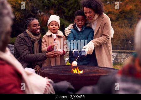 Famille multi-génération ayant plaisir à toaster les guimauves dans le jardin d'automne ensemble Banque D'Images