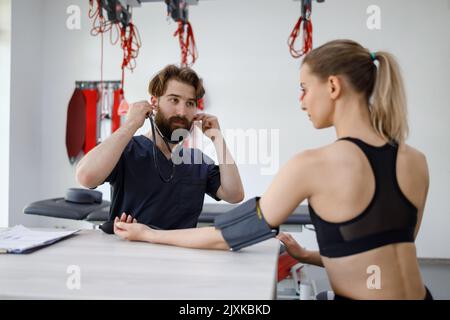 Médecin sportif masculin vérifiant la tension artérielle de l'athlète féminine. Jeune femme de fitness à l'examen médical au physiothérapeute du médecin Banque D'Images