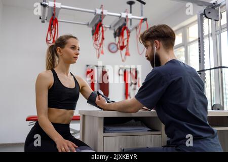 Le médecin physiothérapeute mesure la pression artérielle d'une jeune femme sportive dans un bureau pour l'exercice et la réadaptation Banque D'Images