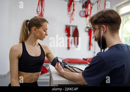 Femme athlétique qui fait l'objet d'un examen médical dans une clinique de réadaptation. Le médecin mesure la pression artérielle d'une fille après un exercice physique Banque D'Images