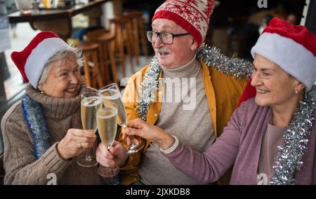 Des amis seniors heureux à l'intérieur dans un café qui se trinquent avec des verres à champagne et fêtent Noël. Banque D'Images