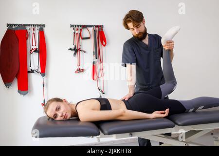 Patiente faisant des exercices physiques avec un physiothérapeute. Spécialiste de la réadaptation masculine traitant le genou blessé d'un athlète. Concept de post traumatot Banque D'Images
