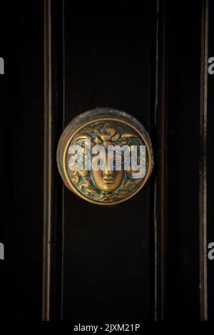 Photo verticale d'un ancien bouton de porte avec la conception d'une tête femelle recouverte de patine verte sur une porte en bois noir vintage. Détails de la porte géorgienne. Banque D'Images