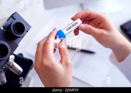Gros plan d'un travailleur de laboratoire effectuant des recherches à l'aide d'un tube à essai portant un microscope étiqueté Omicron Banque D'Images