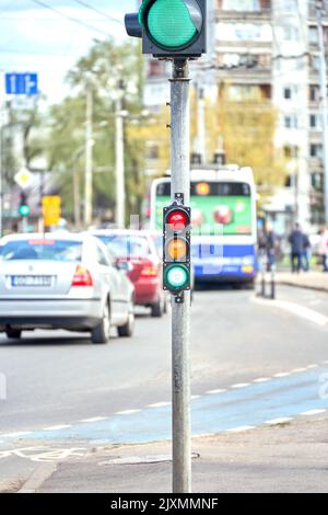 Riga, Lettonie - 13 mai 2022 : petit sémaphore de trafic avec lumière verte sur fond de trafic de la ville. Banque D'Images