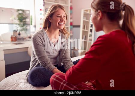 Fille adolescente portant un pyjama assis sur le lit parlant à la mère dans la chambre Banque D'Images