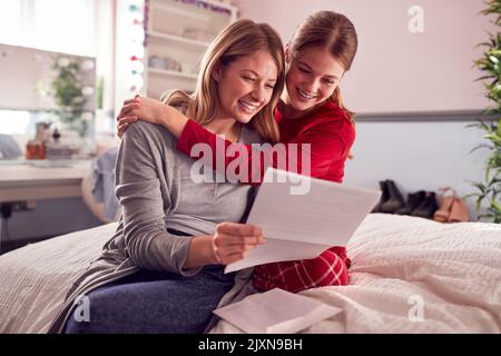 Fille adolescente souriante portant un pyjama regardant le rapport d'examen scolaire avec la mère dans la chambre Banque D'Images