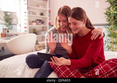 Mère avec une fille adolescente portant un pyjama assis sur le lit faire appel vidéo sur le téléphone mobile Banque D'Images