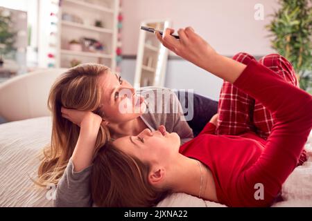 Mère avec fille adolescente portant un pyjama assis sur le lit posant pour Selfie sur le téléphone portable Banque D'Images