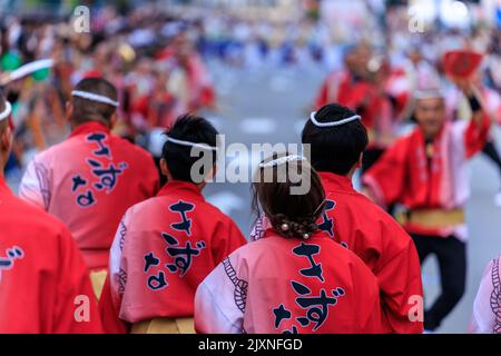 Tokushima, Japon - 12 août 2022: Des artistes en vêtements traditionnels rouge vif regardent le défilé au festival d'Amaodori Banque D'Images