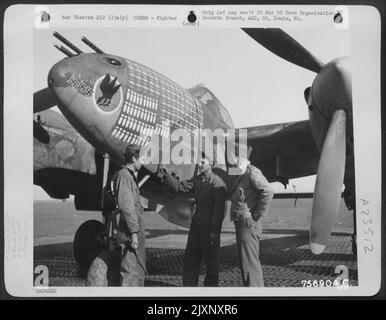 Membres de l'équipage de sol du 94th Escadron de chasseurs, 1st Groupe de chasseurs, discutent des marquages sur le nez d'Un Lockheed P-38 Lightning à leur base en Italie. Banque D'Images