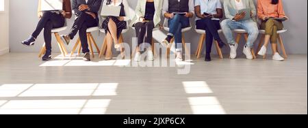 Photo en coupe basse des jambes de personnes diverses qui attendent en file d'attente pour un entretien d'emploi Banque D'Images