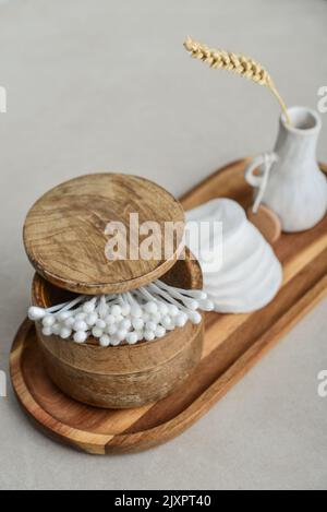 Сotton bourgeons dans une boîte en bois avec des tampons de coton ronds sur plateau en bois sur un fond en béton léger Banque D'Images