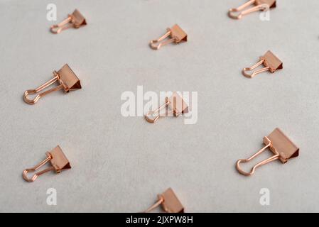 Motif de pinces de reliure en papier doré sur fond en béton clair. Arrière-plan des fournitures de bureau Banque D'Images