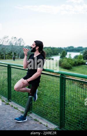 Jeune homme avec une barbe et une jambe prothétique envoyant une note audio avec un smartphone Banque D'Images