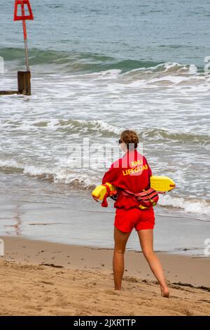 RNLI sauveteur marchant le long d'une plage de sable transportant un flotteur de sauvetage à swanage sur l'île de purbeck à dorset royaume-uni, institution nationale royale de sauvetage Banque D'Images