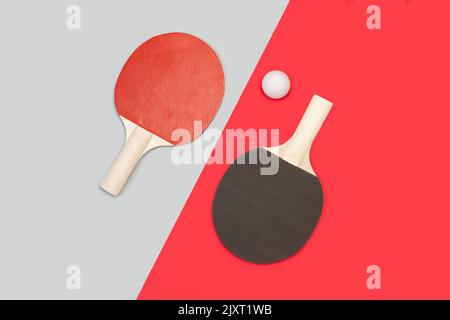 Pagaies de ping-pong rouges et noires avec une balle blanche sur fond gris et rouge Banque D'Images