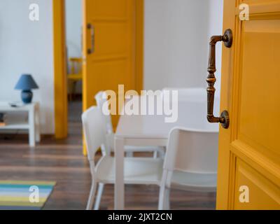 Chambre moderne avec portes jaunes, murs et mobilier blancs, mise au point sélective. Vue du salon par la porte entrouverte Banque D'Images