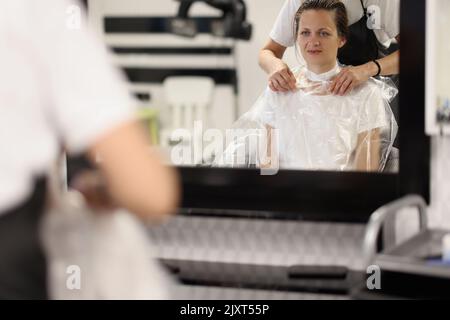 La coiffeuse met un sac en papier autour du cou de la femme pour protéger les vêtements qu'elle coupe les cheveux à l'intérieur Banque D'Images