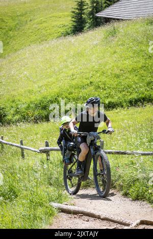 L'homme fait monter son e-bike sur une piste de montagne escarpée avec un jeune enfant à l'arrière dans un siège pour enfant, en Italie Banque D'Images
