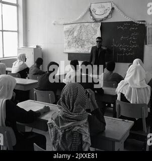 1960s, historique, éducation, garçons arabes assis à des bureaux en bois dans une salle de classe, certains avec le casque traditionnel, connu sous le nom de keffiyeh, Jeddah, Arabie Saoudite. Banque D'Images