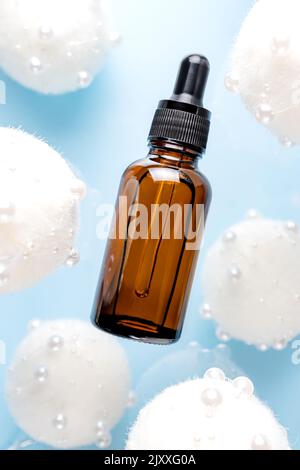 Huile pour le visage de beauté avec huile essentielle naturelle, hyaluron, vitamine C décorée de boules étincelantes blanches de fête sur fond bleu. La lévitation Banque D'Images