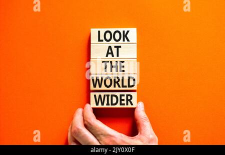 Regardez le symbole du monde entier. Les mots de concept regardent le monde plus large sur des blocs de bois sur un magnifique fond orange. Main d'homme d'affaires. Affaires an Banque D'Images