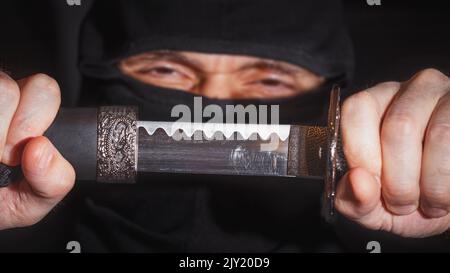 Ninja prêt à combattre, tenant une épée japonaise.Photo d'un guerrier vêtu de vêtements noirs et d'un visage fermé Banque D'Images