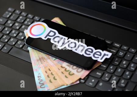 TERNOPIL, UKRAINE - 6 SEPTEMBRE 2022 le logotype de papier Payoneer repose sur un clavier noir pour ordinateur portable avec des factures hryvnia ukrainiennes. Payoneer est américain Banque D'Images