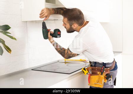 Male Worker Fixing Kitchen Hood With Screwdriver In Kitchen Stock Photo