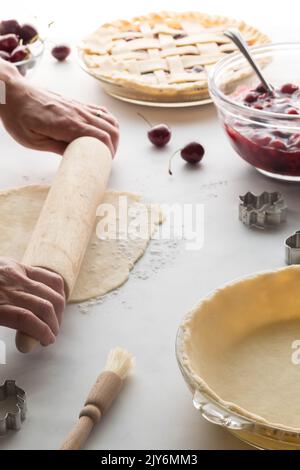 Les mains roulent la pâte en préparation d'une tarte fraîche à la cerise. Banque D'Images