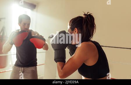 Boxeur féminin ayant une session d'entraînement avec son entraîneur dans un anneau de boxe. Une jeune femme sportive qui fait des étincelles avec son entraîneur personnel à la salle de gym. Banque D'Images