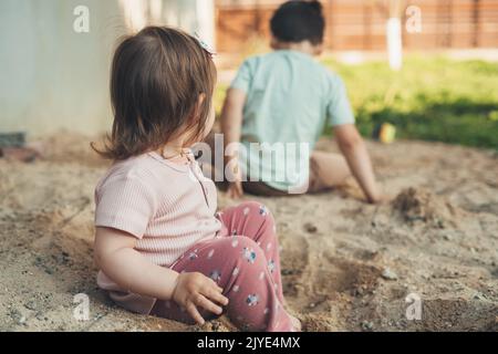 Petite fille blanche avec son frère creusant le trou dans le sable le jour du printemps. Activités d'été en plein air. Bonne famille. Vacances d'été. Banque D'Images