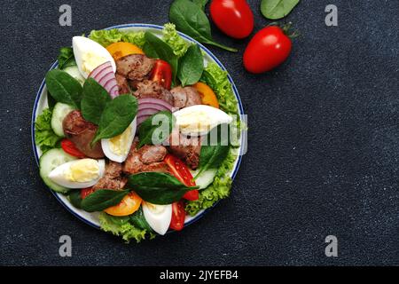 Salade Périgord avec foie de poulet, tomates, concombres, œufs, laitue et épinards. Arrière-plan de la table de cuisine noire, vue du dessus Banque D'Images