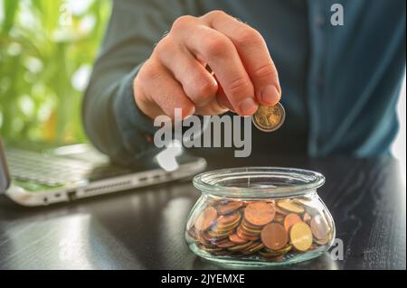 Sur un bureau, les pièces en euros sont symboliquement placées dans un pot par un homme d'affaires pour économiser de l'argent Banque D'Images