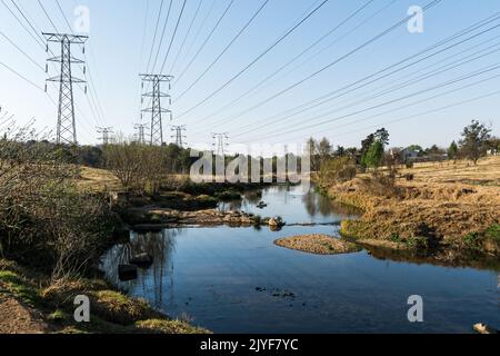 Transmission électrique lignes électriques aériennes traversant un cours d'eau idyllique dans un espace vert urbain Banque D'Images