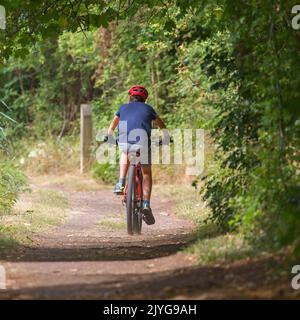 Vue arrière d'un garçon sur son vélo isolé le long d'un canal rural du Royaume-Uni, chemin de remorquage portant un casque de vélo. Banque D'Images